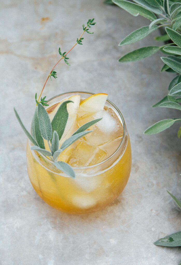 Closeup of pear cocktail, surrounded with sprigs of fresh sage.