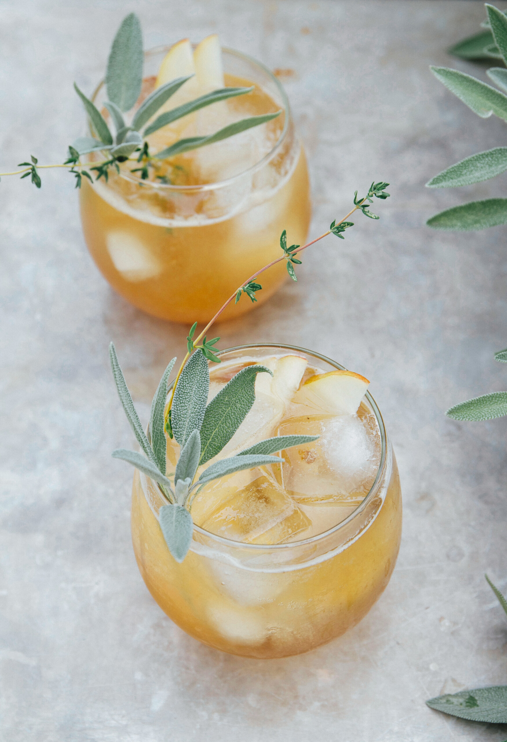 Two cocktails with pears, sage, and thyme leaves.